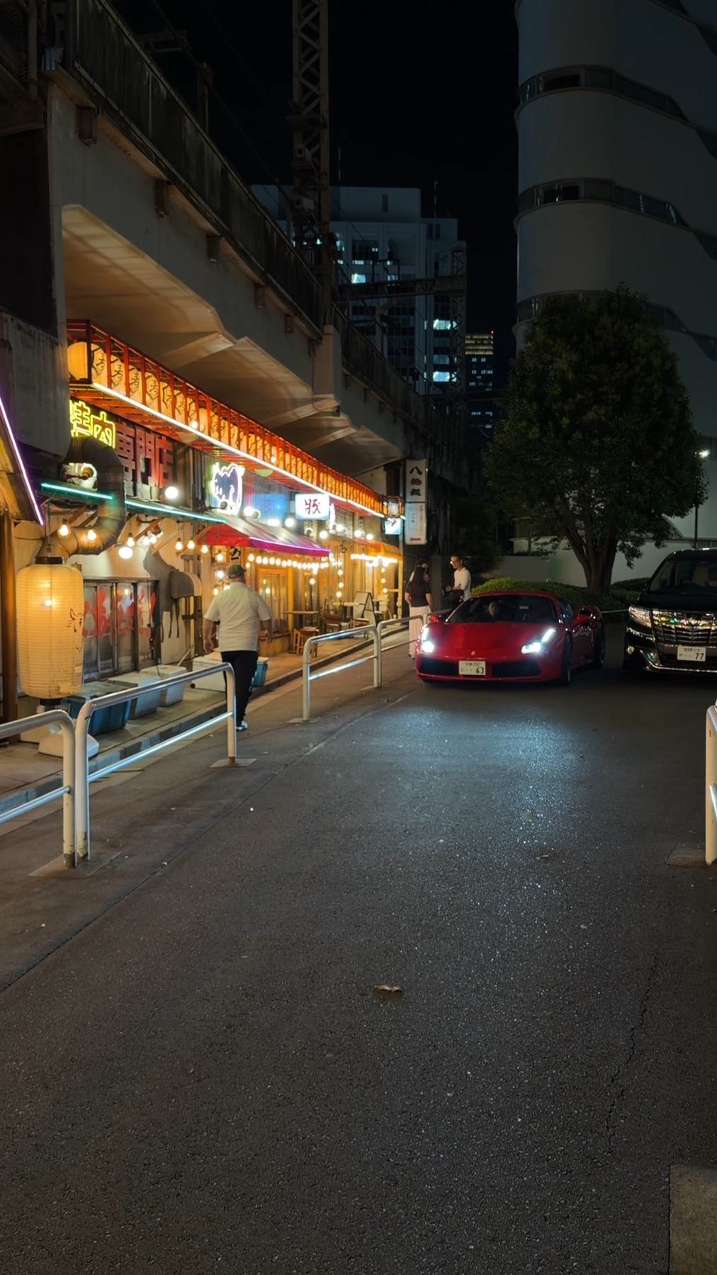 Red Ferrari 488 GTB on a Tokyo street at night, lit by red lanterns beneath an elevated railway